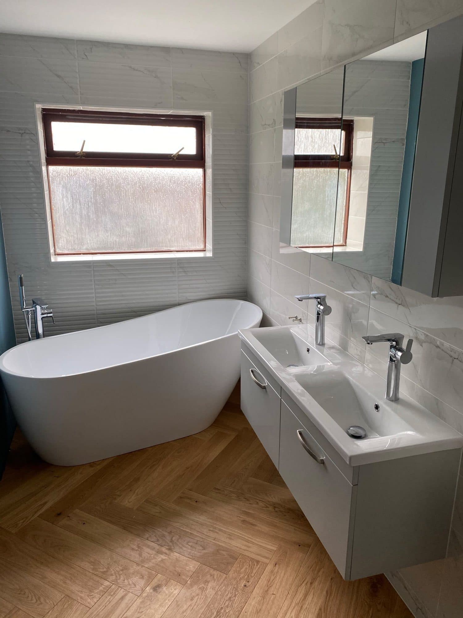 A freestanding bath and wall-hung vanity unit on a herringbone wood floor