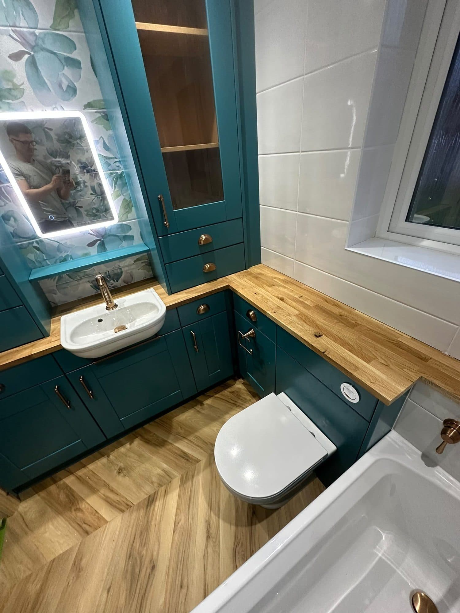 A teal bathroom with fitted units, a backlit mirror and a herringbone floor