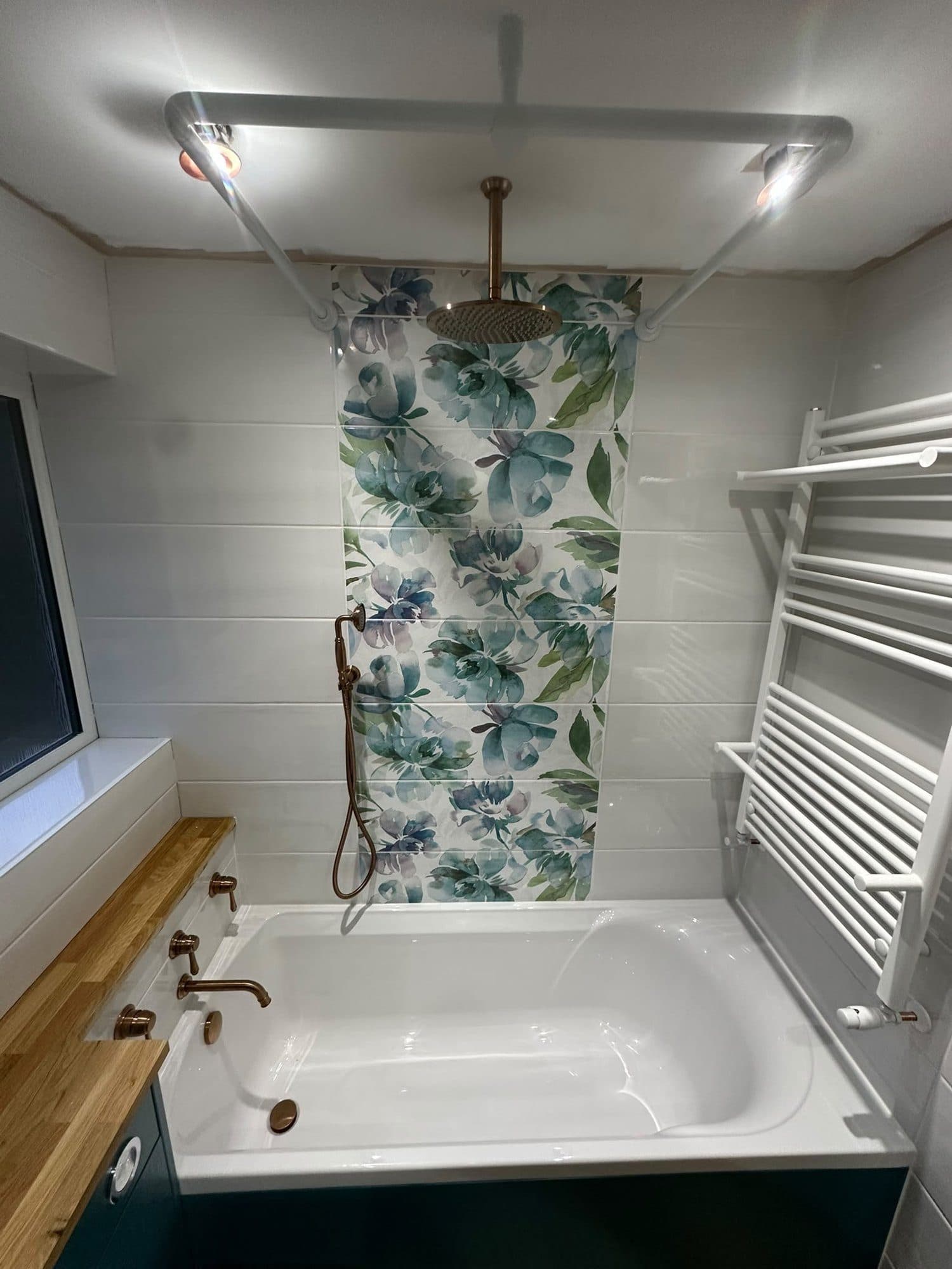 A bath with a floral feature panel, a chrome towel radiator and a wood-effect floor