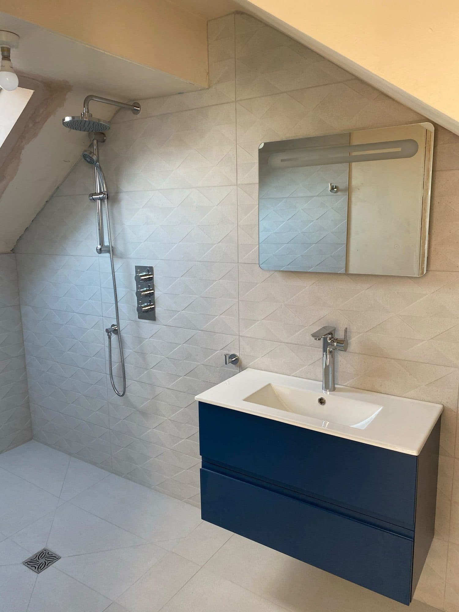 A loft shower room with a navy vanity unit and a mirror cabinet