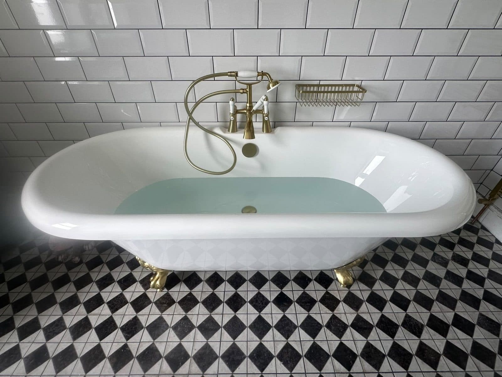 A roll-top bath with brass taps, white metro tiles and a black and white patterned floor
