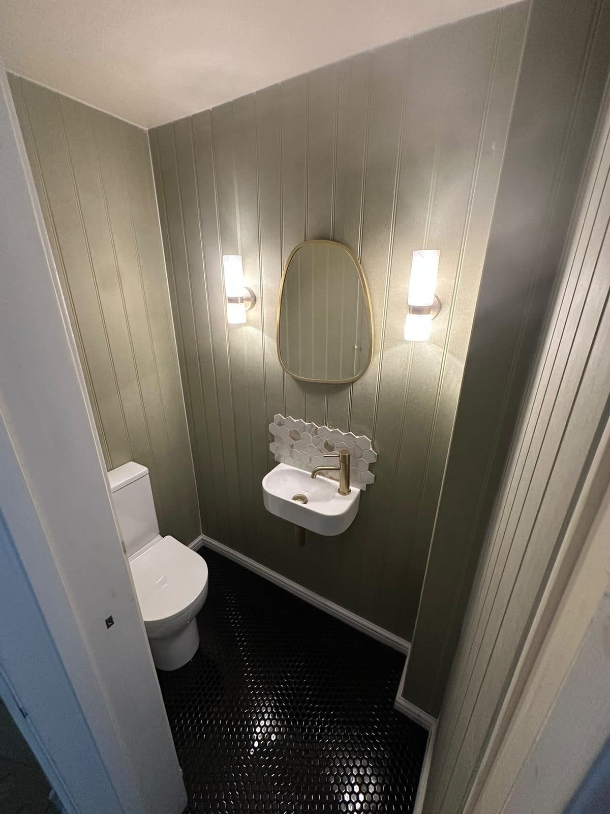 A cloakroom with green wall panelling, a dark tiled floor and wall lights