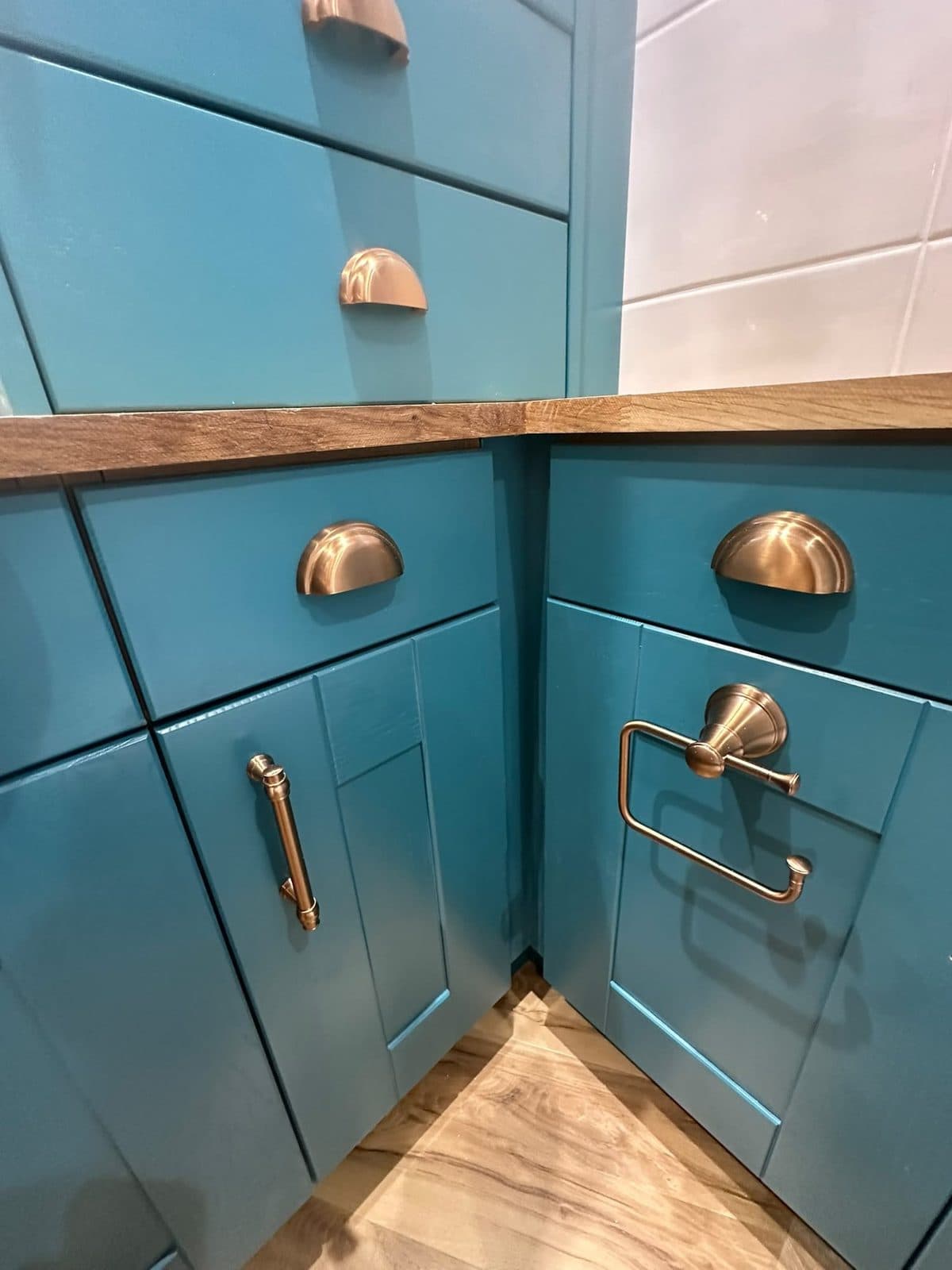 A teal cabinet with copper-coloured handles under an oak worktop