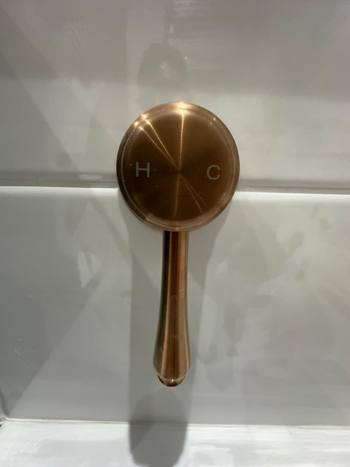 A copper-coloured shower control on white wall tiles