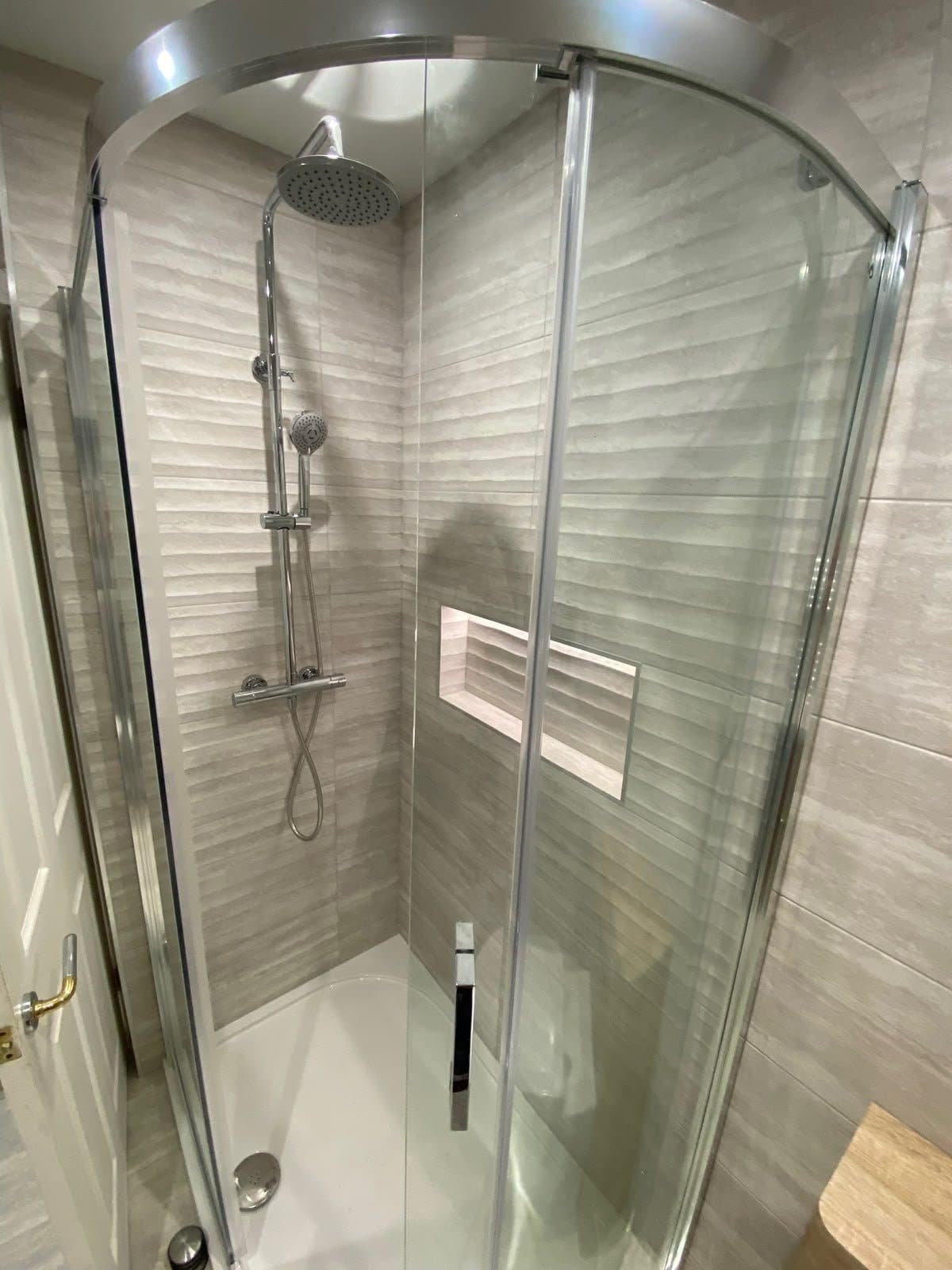 A walk-in shower enclosure with grey tiles and a tiled niche