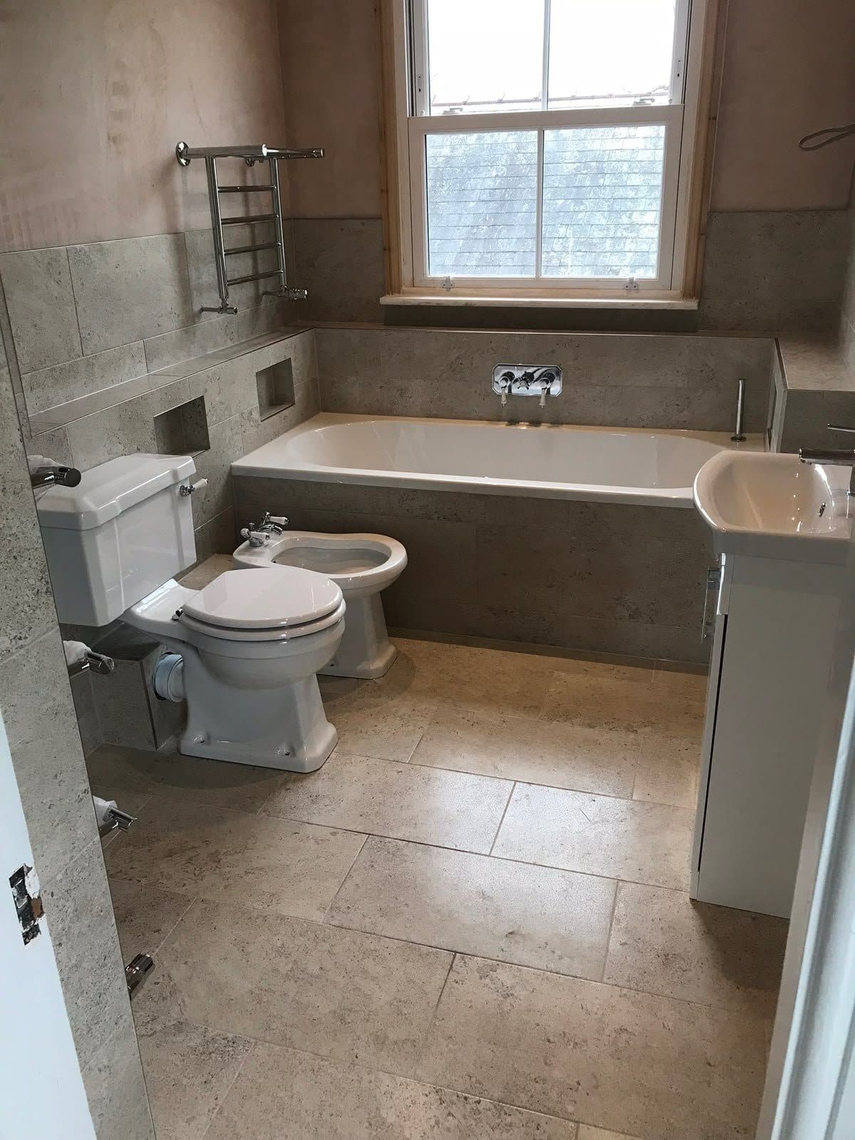 A bathroom with a bath, toilet and basin under a window